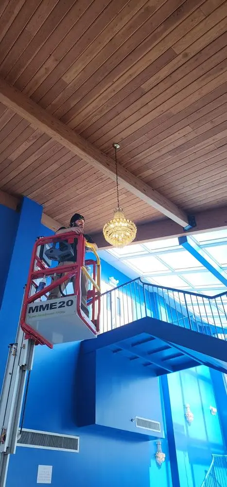 Electrician on a lift installing a chandelier under a wood ceiling